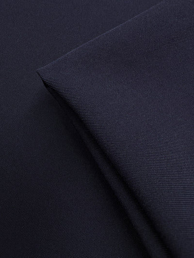 A close-up of Super Cheap Fabrics' Liquid Twill - Black Iris (150cm) highlights its dark navy blue color and distinct diagonal weave, with one section folded neatly over another.