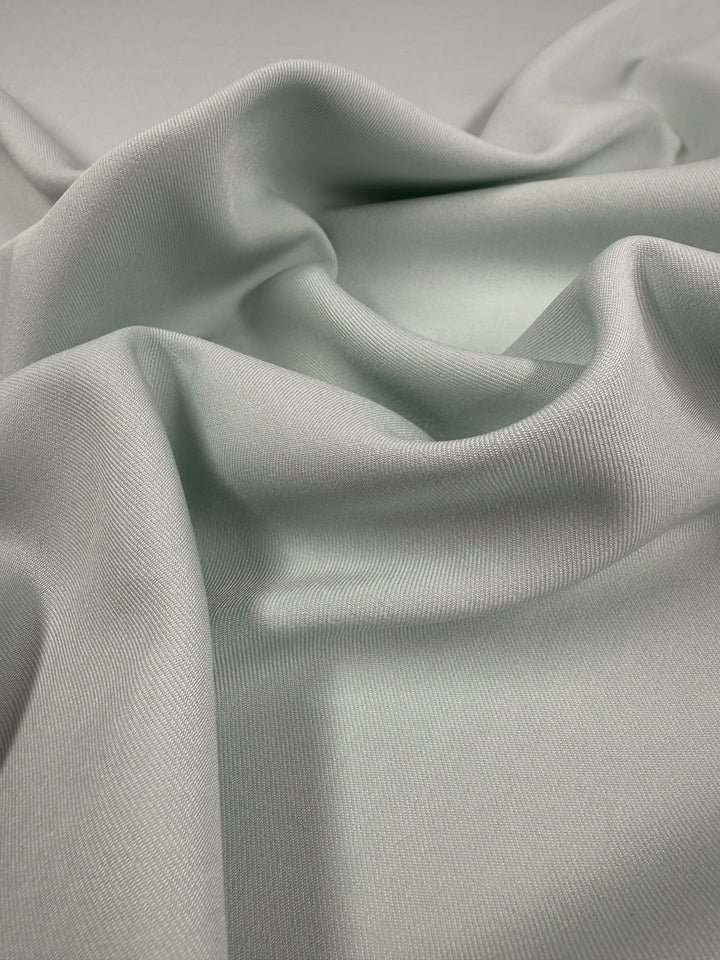 Super Cheap Fabrics' Liquid Twill - Murmur (150cm) is a light gray, medium-weight twill fabric with a smooth, satin-like texture that drapes in soft, flowing folds for elegant highlights and shadows.