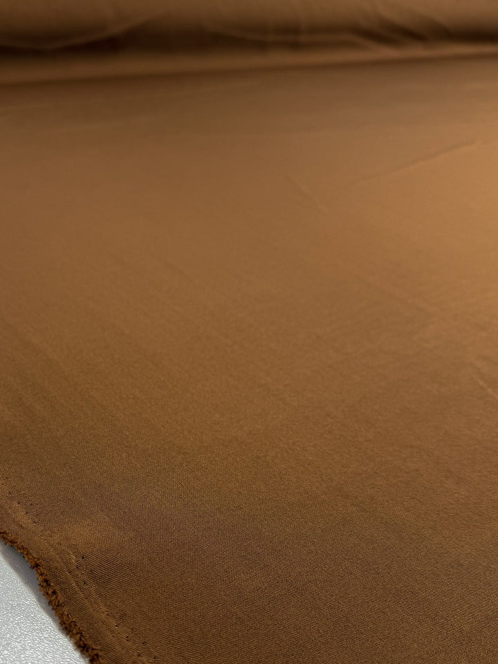 A close-up of Super Cheap Fabrics’ Liquid Twill in Caramel Cafe (150cm), showing its smooth, medium weight twill texture with slightly frayed edges and even lighting across the soft, brown suiting fabric.