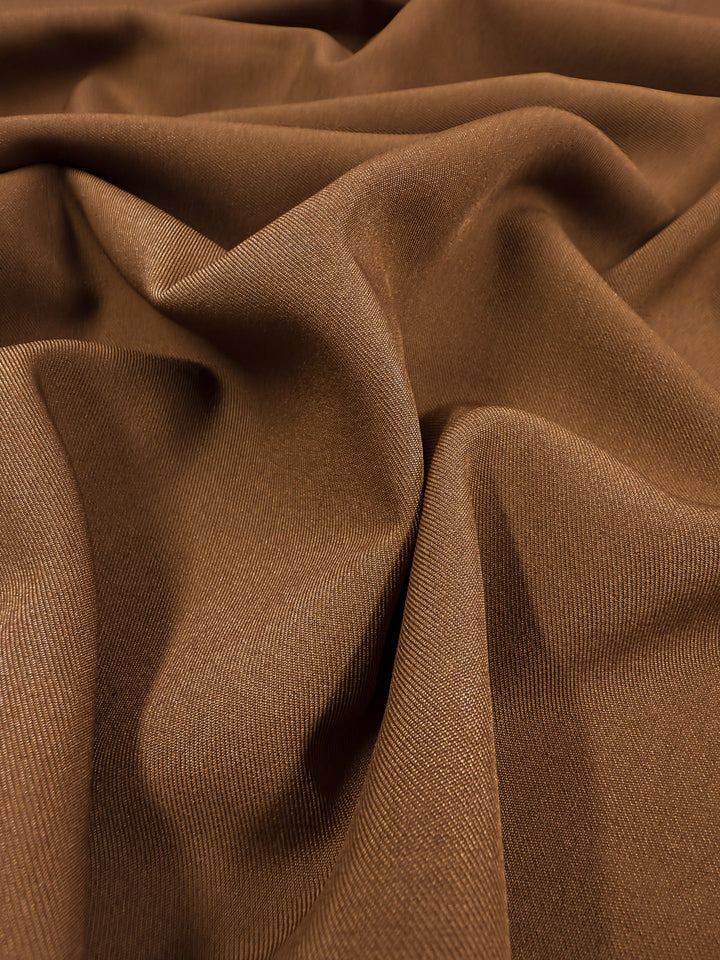 A close-up of Super Cheap Fabrics' Liquid Twill - Caramel Cafe (150cm) highlights its soft, caramel-brown surface with a smooth texture and gentle folds, forming flowing curves and shadows.