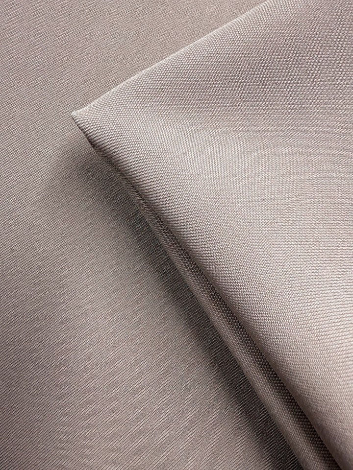 Close-up of Liquid Twill - Goat - 150cm from Super Cheap Fabrics, featuring smooth, finely woven taupe polyester with one piece neatly folded over another to highlight its premium texture.