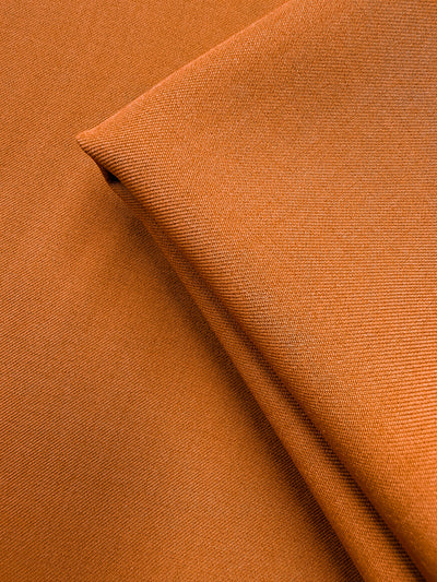 Close-up of Liquid Twill - Tomato Cream (150cm) by Super Cheap Fabrics, featuring neatly folded orange fabric with a subtle textured weave, smooth soft polyester, and fine stitching details.