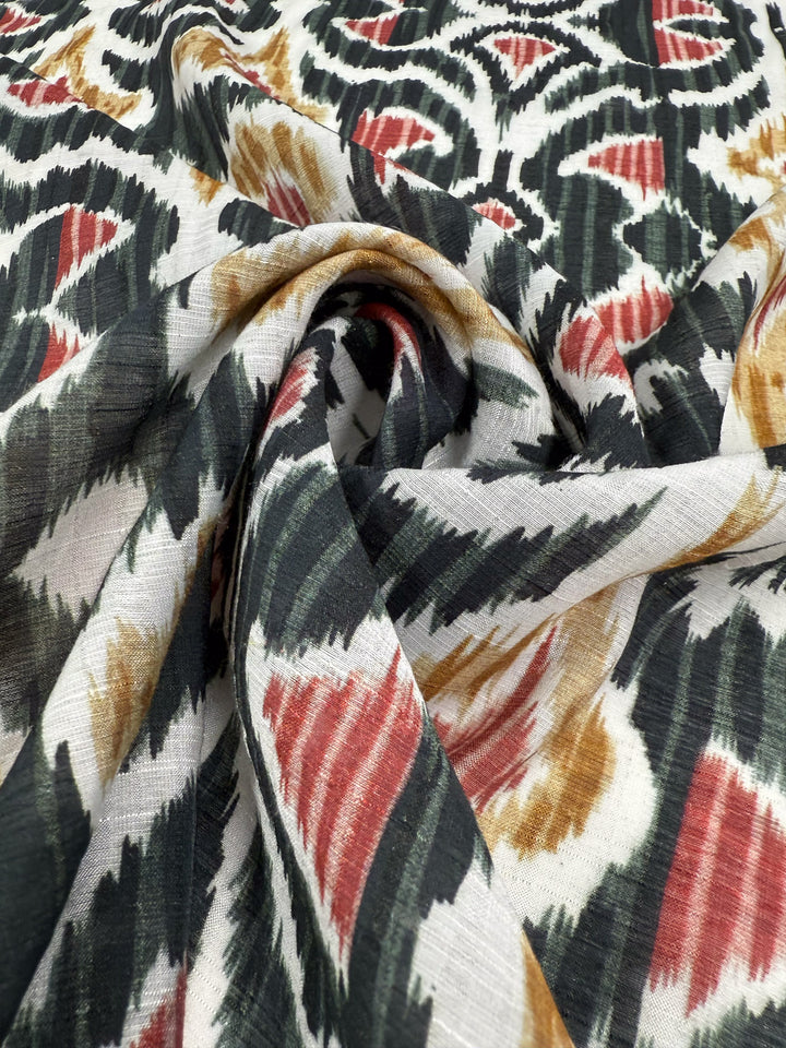 A close-up of Super Cheap Fabrics' Textured Designer Cotton - Spice Loom (150cm), showing a swirling fold with black, white, red, and brown abstract Ikat-style patterns.