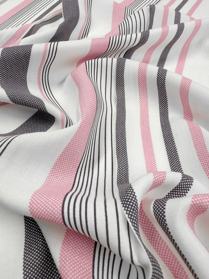 A close-up of Super Cheap Fabrics' Printed Rayon - Candy Noir Stripe (140cm), showing black, pink, and white horizontal stripes on lightweight fabric with a soft texture, slight drape, gentle wrinkles, and a woven pattern.