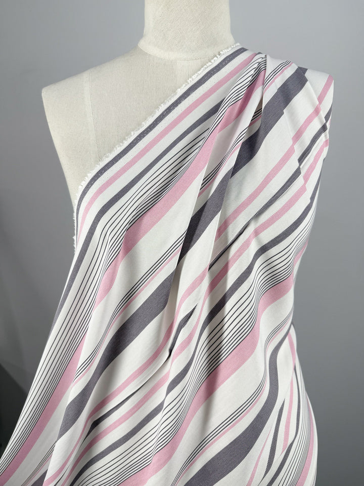 Super Cheap Fabrics' Printed Rayon - Candy Noir Stripe (140cm) in pink, black, and white drapes over a dress form's shoulder, showcasing its lightweight feel against a plain, neutral background.