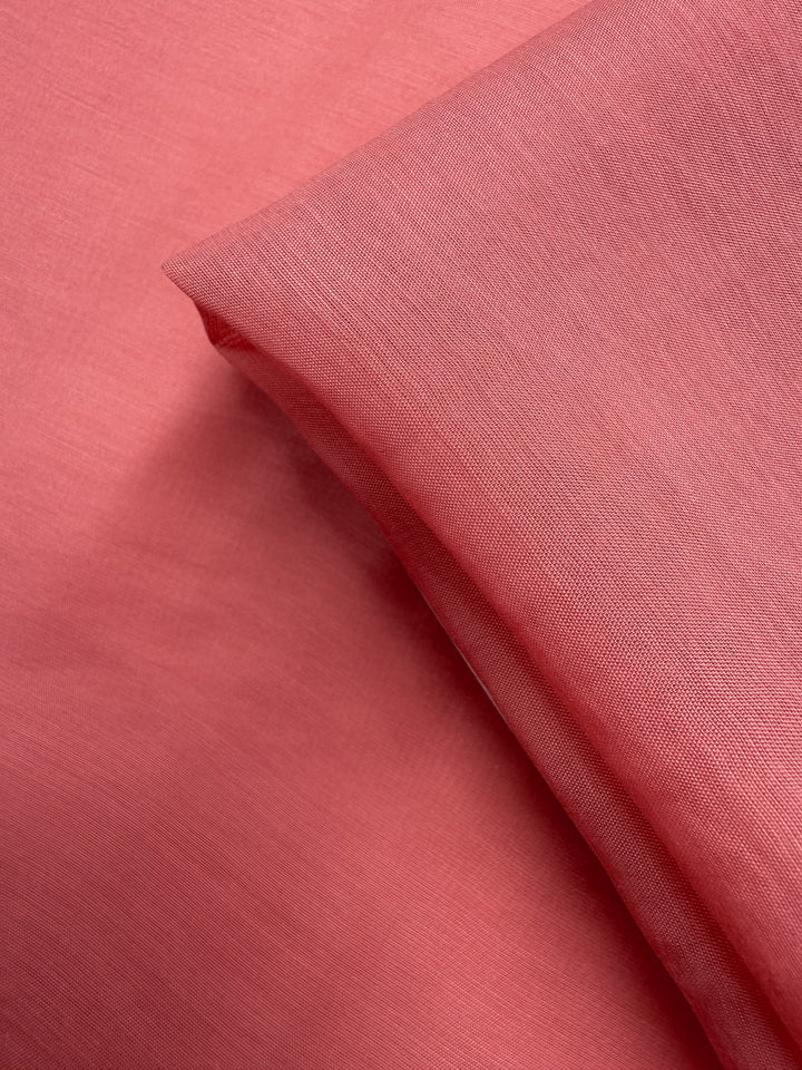 A close-up of Super Cheap Fabrics’ Designer Voile - Rose of Sharon - 150cm reveals its fine, slightly sheer pink texture. The lightweight fabric is softly folded, showing gentle shadows—ideal for summer dresses.