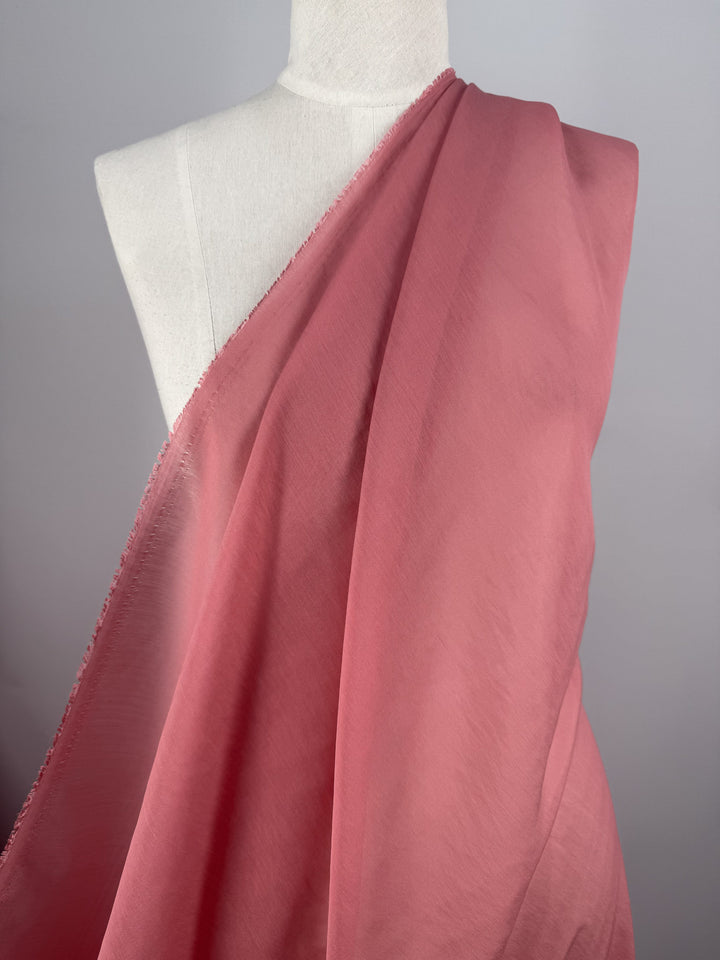 A mannequin showcases Super Cheap Fabrics' Designer Voile - Rose of Sharon - 150cm, draped diagonally over the torso against a gray background—ideal for inspiring summer dresses with this airy, rose-pink fabric.