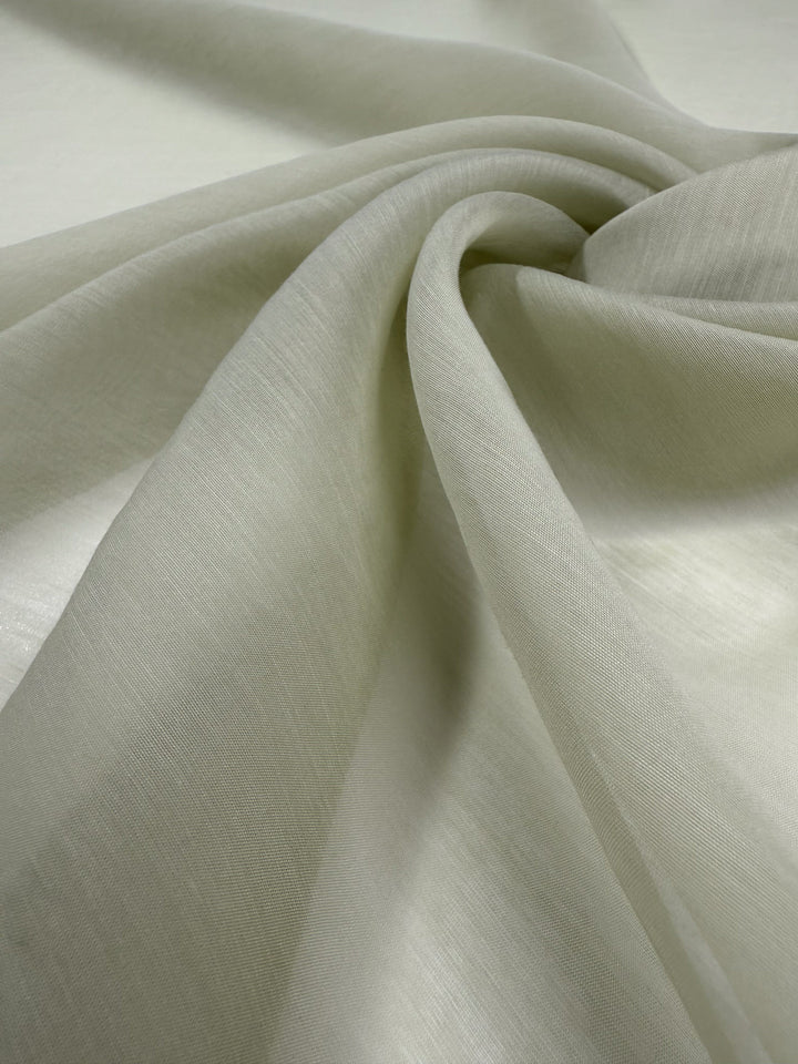 A close-up of Designer Voile - White Jade - 150cm by Super Cheap Fabrics, showing its light beige, sheer cotton nylon fabric draped in soft folds and twists to highlight the delicate texture and semi-transparency.