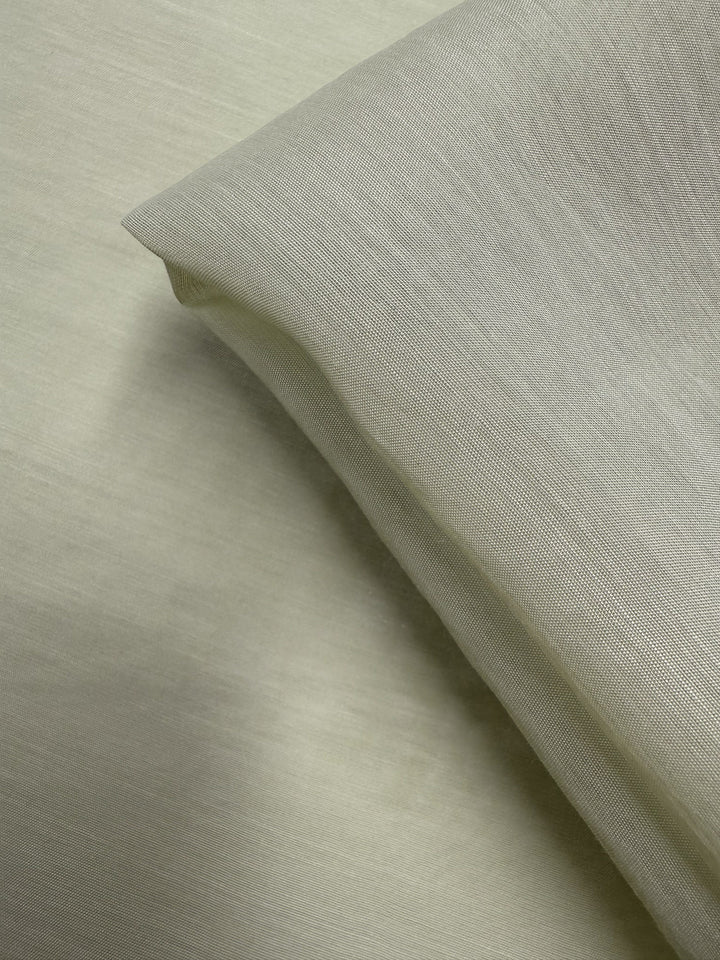 A close-up of Designer Voile - White Jade - 150cm by Super Cheap Fabrics, showcasing its sheer, lightweight cotton nylon blend with a smooth, subtly textured surface draped at an angle over a matching background.