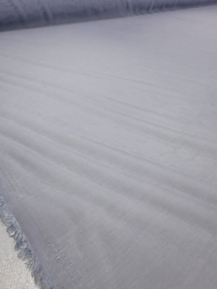 A close-up of Super Cheap Fabrics' Designer Voile - Skywriting - 150cm shows its smooth, light purple lightweight fabric with soft folds and frayed edges along the left side.