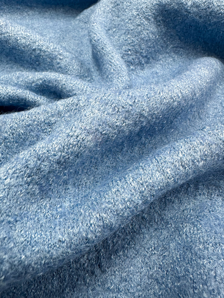 Close-up of Super Cheap Fabrics' Boiled Wool - Allure (150cm), showcasing its textured, fuzzy surface in a soft, light blue wool-viscose blend. The slightly crumpled material creates gentle folds for a cozy look.