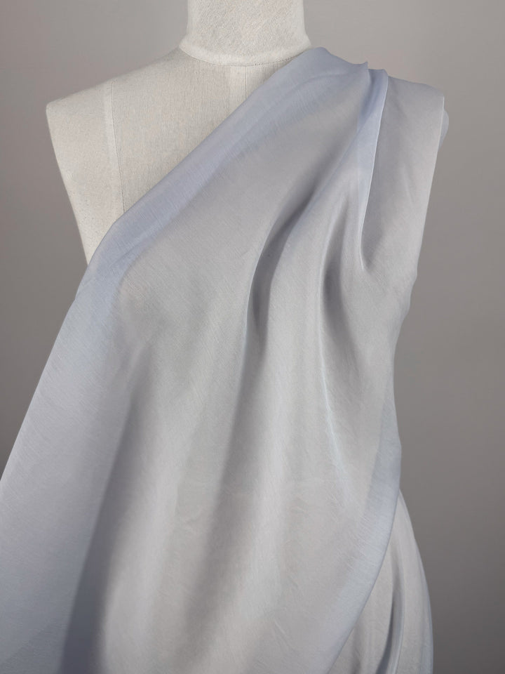 Designer Voile - Skywriting - 150cm by Super Cheap Fabrics, a light blue semi-sheer fabric, is draped diagonally over the shoulder and torso of a white dress form against a neutral background.