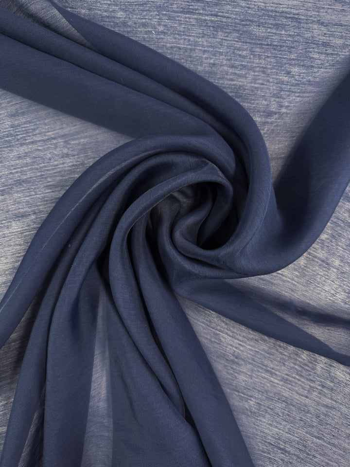 A close-up of Super Cheap Fabrics' Designer Voile - Pageant Blue (150cm), softly twisted into a spiral on a light surface. This lightweight, semi-transparent fabric is perfect for airy summer dresses.