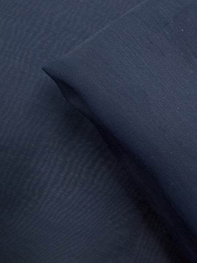 A close-up of Super Cheap Fabrics' Designer Voile - Pageant Blue (150cm), showing one piece laid flat and another folded to highlight its fine weave and lightweight texture, ideal for breezy summer dresses.
