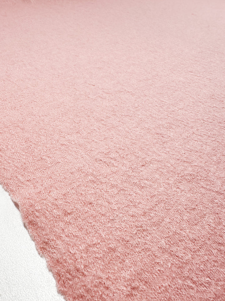 Close-up of Super Cheap Fabrics' Boiled Wool in Powder Pink, 145cm wide, showcasing a textured fabric crafted from a wool-viscose blend with a soft surface. A white edge is visible on the left, highlighting its luxurious detail.