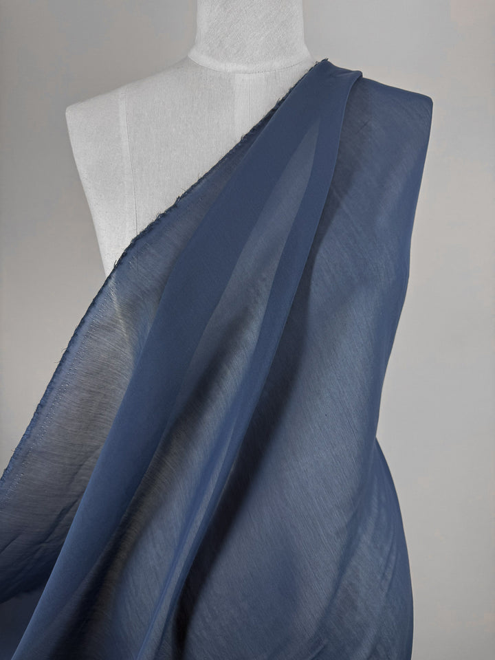 A close-up of a dressmaker’s mannequin draped with Super Cheap Fabrics’ Designer Voile - Pageant Blue- 150cm over one shoulder against a neutral background—ideal for crafting elegant summer dresses.