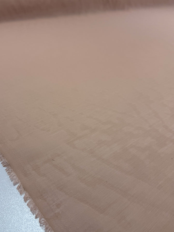 A close-up of Super Cheap Fabrics’ Designer Voile - Apple Blossom (150cm), a light beige, lightweight fabric with subtle geometric patterns and a frayed left edge. The soft surface has a slight sheen, highlighting its quality.