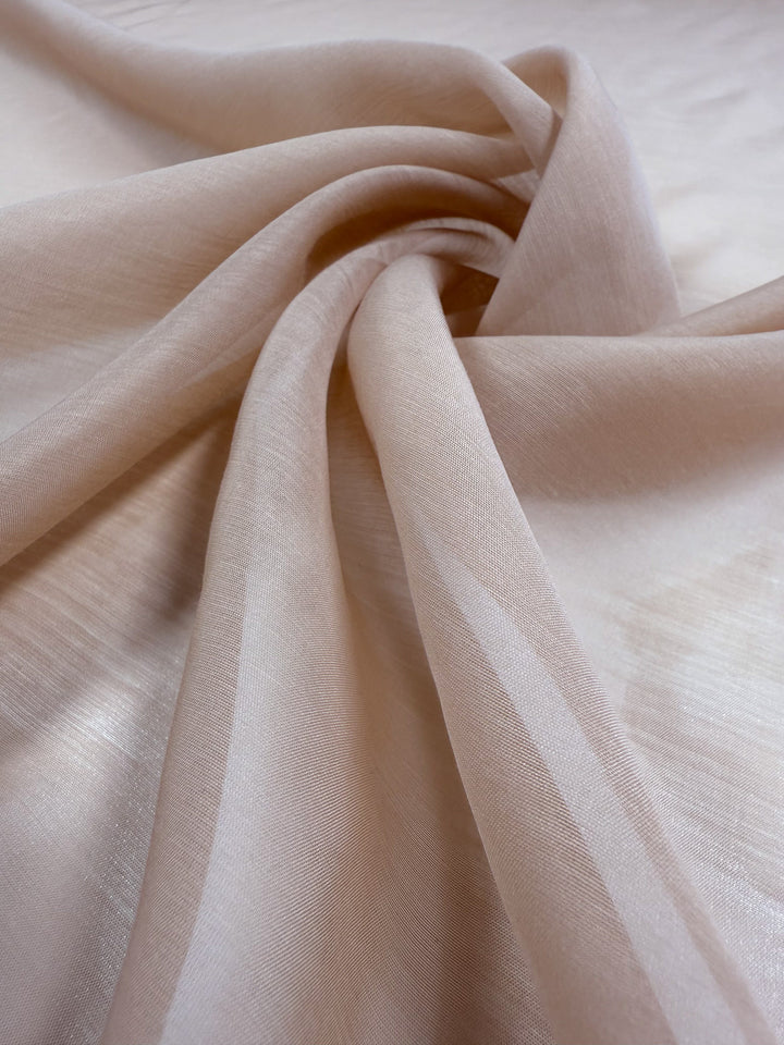 A close-up of Designer Voile - Apple Blossom - 150cm by Super Cheap Fabrics shows its light beige, sheer fabric gathered in soft folds, highlighting a smooth texture and slightly translucent quality.