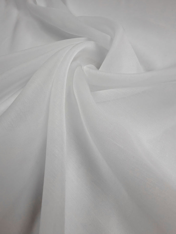 A close-up of Super Cheap Fabrics’ Designer Voile - White - 150cm shows soft folds and gentle draping, highlighting its smooth, semi-transparent, and elegant texture.
