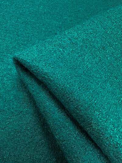 A close-up of the teal Boiled Wool - Everglade fabric by Super Cheap Fabrics, featuring a soft, textured surface. The wool-viscose blend appears thick and luxurious, forming gentle folds and shadows. Width: 135cm.