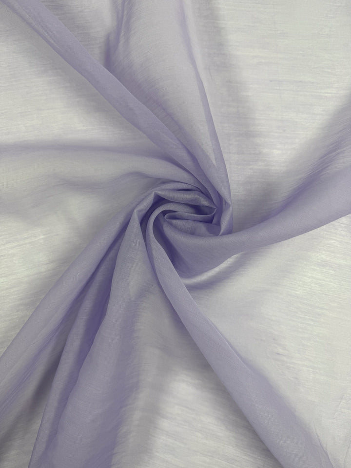 The Designer Voile - Pastel Lilac - 150cm from Super Cheap Fabrics is a sheer fabric, softly twisted to form gentle folds and an airy look, with its translucent lilac hue standing out against a neutral backdrop.