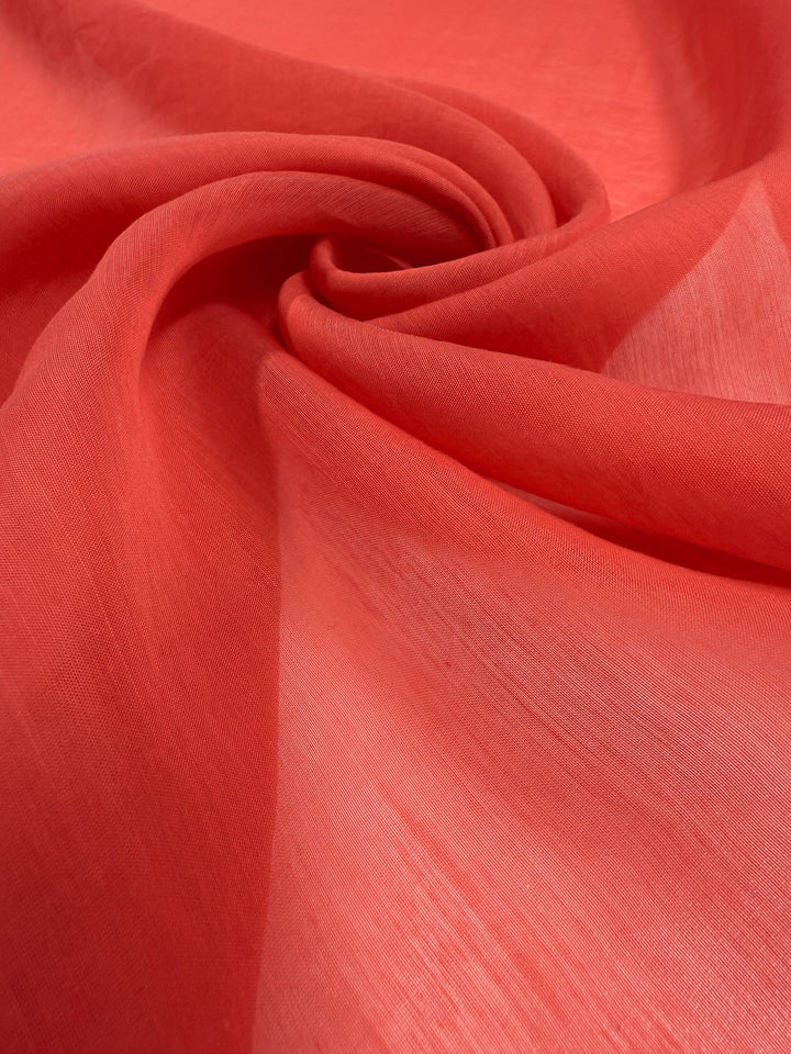 A close-up of Super Cheap Fabrics’ Designer Voile - Paprika - 150cm shows its lightweight, sheer and flowing texture gently twisted into a spiral—ideal for airy summer dresses.