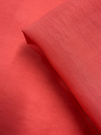 A close-up of Super Cheap Fabrics' Designer Voile - Paprika (150cm) shows its soft, slightly sheer texture and smooth, lightweight look, neatly folded—ideal for summer dresses.