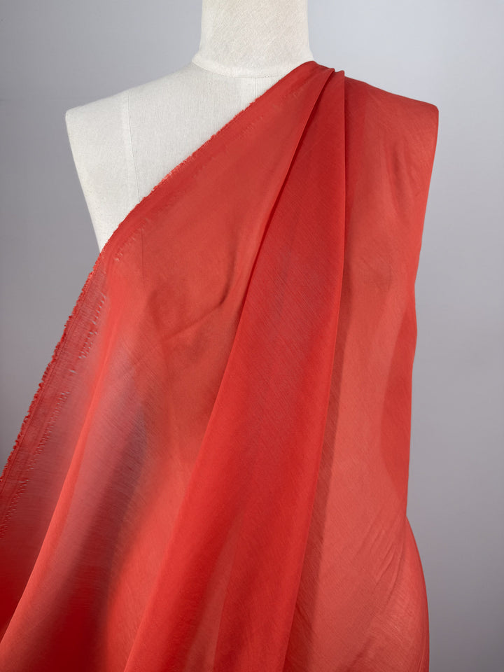A mannequin displays Super Cheap Fabrics’ Designer Voile - Paprika - 150cm, a smooth, lightweight, slightly translucent red fabric shown from the shoulders down against a plain gray background, perfect for elegant sheer summer dresses.