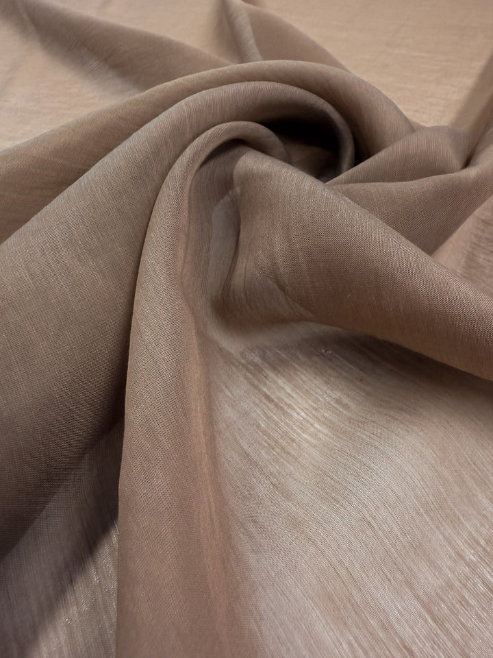 A close-up of Super Cheap Fabrics' Designer Voile - Burro - 150cm, an extra lightweight, sheer light brown fabric arranged in soft folds to highlight its smooth texture and semi-transparency.