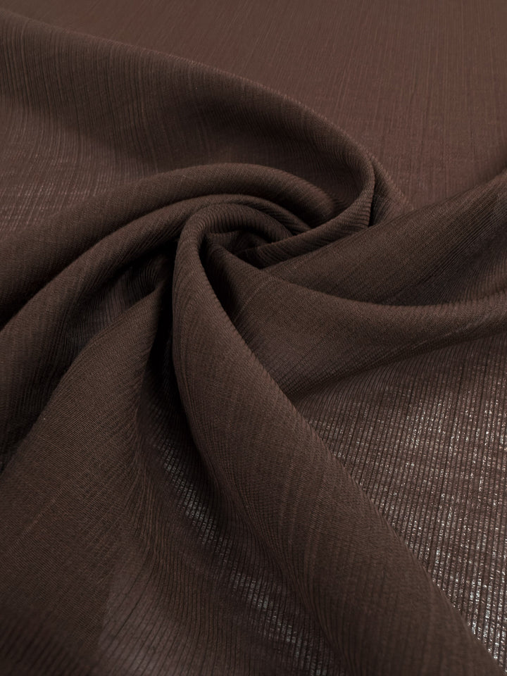 A close-up of Super Cheap Fabrics' Textured Designer Voile - French Roast (155cm), gently twisted to highlight its soft drape, subtle textured pattern, and semi-transparency—perfect as a lightweight summer fabric.