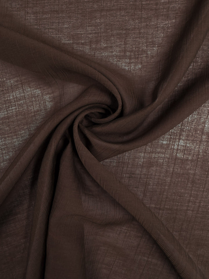 Close-up of Super Cheap Fabrics’ Textured Designer Voile - French Roast - 155cm, featuring soft brown fabric gathered at the center for swirling folds and gentle texture, allowing light to softly filter through.