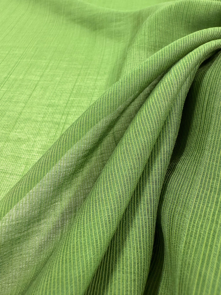 A close-up of Super Cheap Fabrics' Textured Designer Voile - Salted Lime (155cm) shows a fine, lightweight weave with subtle diagonal lines and gentle folds, ideal for summer garments.
