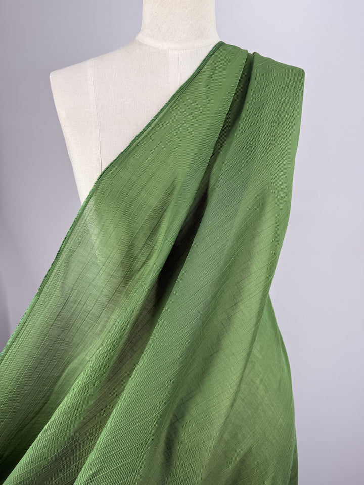 A close-up of a mannequin wearing Super Cheap Fabrics' Textured Designer Voile - Salted Lime - 155cm, with the sheer green fabric draped diagonally over one shoulder, shown from the back against a plain light background.
