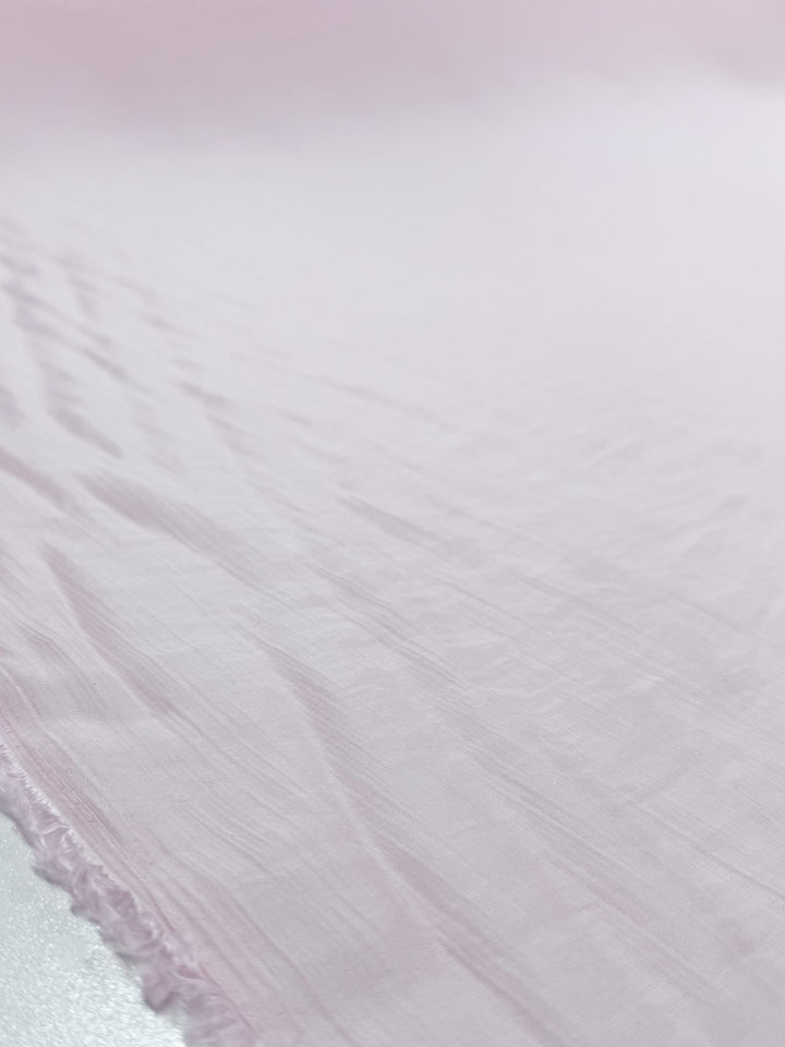 Close-up of Super Cheap Fabrics' Textured Designer Voile - Carinaria (155cm): a soft, light pink cotton with a slightly crinkled texture, subtle wrinkles and frayed edge—ideal for sheer summer dresses or creative voile projects.