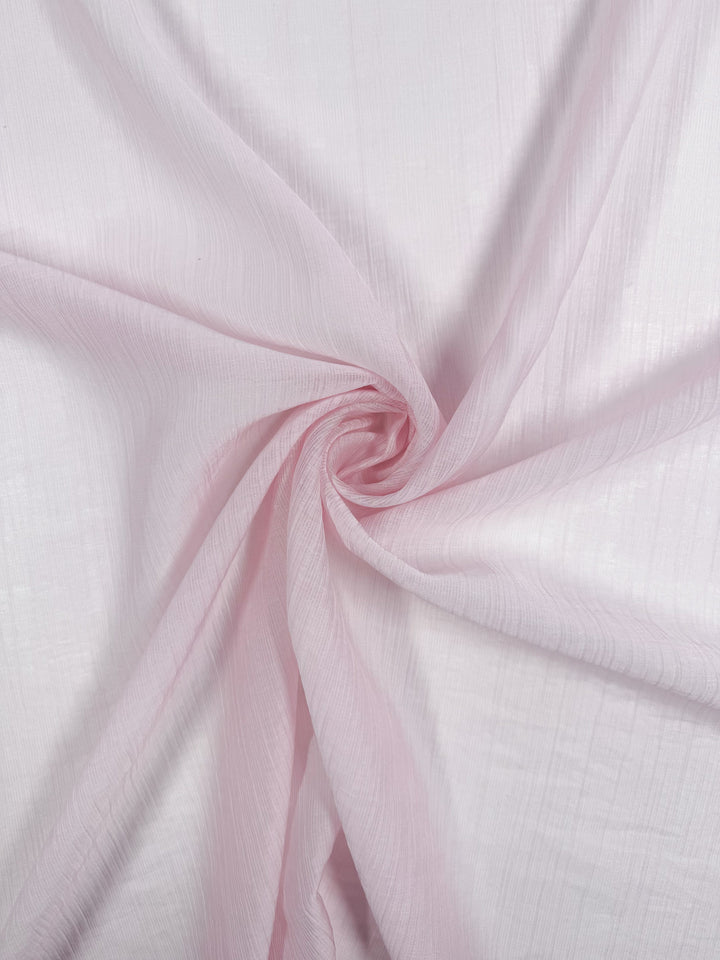 Textured Designer Voile - Carinaria by Super Cheap Fabrics features a light pink, sheer material with soft folds and ripples. Its airy translucency and delicate texture are highlighted against a light background. Width: 155cm.