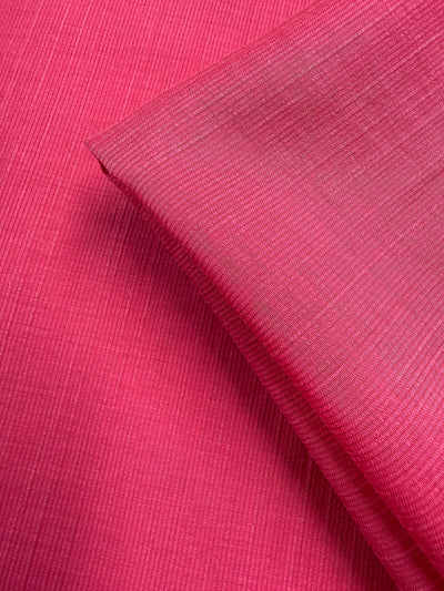 A close-up of Super Cheap Fabrics’ Textured Designer Voile - Raspberry Sorbet (155cm) shows two pieces—one flat, one folded—emphasizing the lightweight ribbed texture and intricate weave of this vibrant fabric.