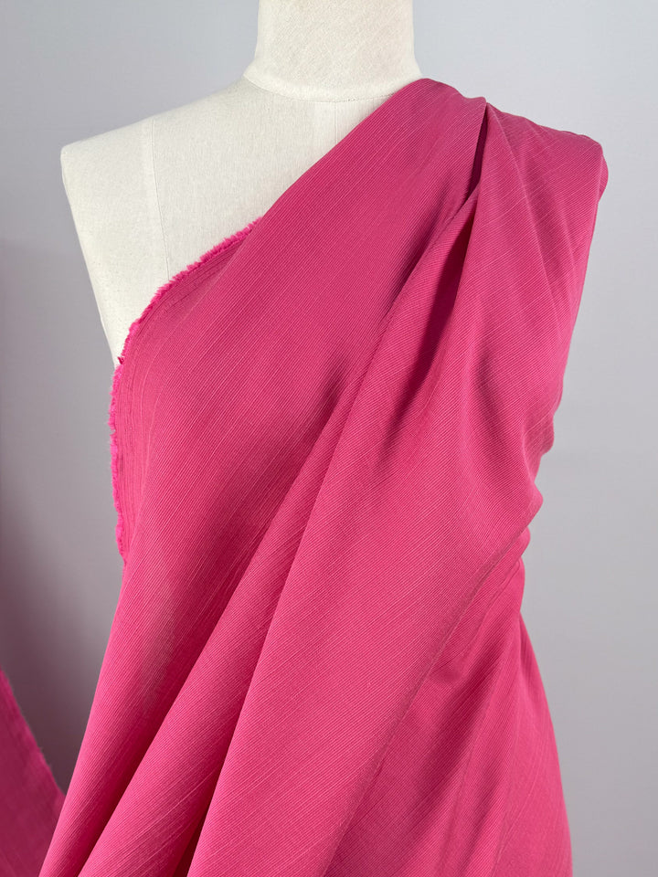 A mannequin is shown from shoulders to mid-torso, draped in Super Cheap Fabrics' Textured Designer Voile - Raspberry Sorbet - 155cm, with the lightweight pink fabric wrapped diagonally across the chest against a plain light grey background.