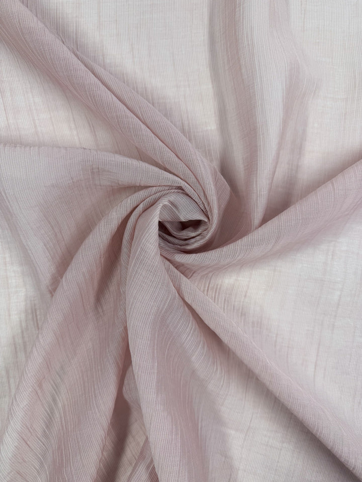 A close-up of Super Cheap Fabrics’ Textured Designer Voile - Sepia Rose (155cm), featuring sheer light pink fabric with subtle stripes, softly gathered at the center—ideal for creating elegant summer dresses.