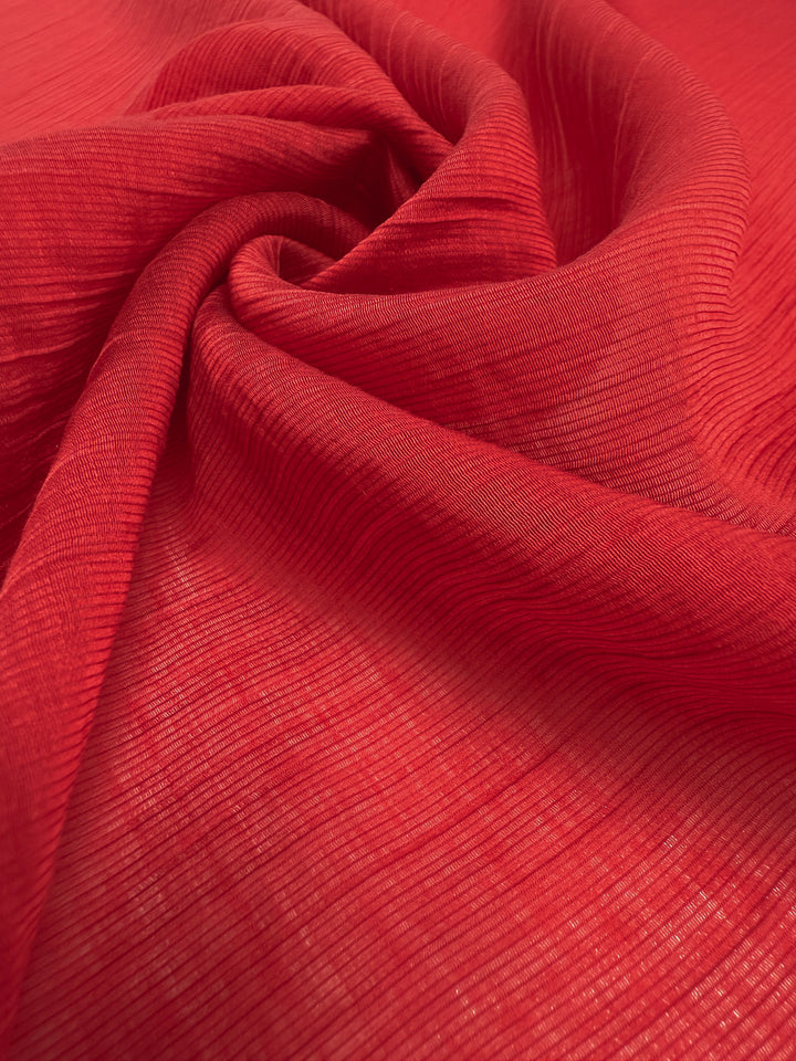 A close-up of Super Cheap Fabrics' Textured Designer Voile - True Red (155cm), showcasing its wavy, crinkled pattern gathered into a loose spiral fold.