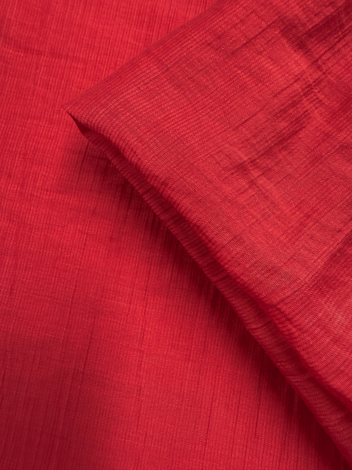A close-up of Super Cheap Fabrics' Textured Designer Voile - True Red (155cm) shows its lightweight, finely textured weave. A folded section casts a soft shadow, highlighting the delicate detail and summer appeal of this fabric.