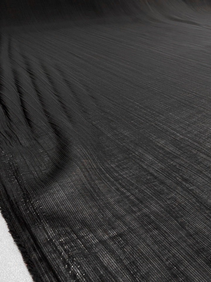 A close-up of Super Cheap Fabrics’ Textured Designer Voile - Black - 155cm reveals its woven, textured pattern with subtle horizontal lines and a gentle sheen, perfect for sheer summer dresses.