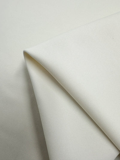 Close-up of a piece of folded Milano Ponte - Ivory - 145cm fabric by Super Cheap Fabrics, showcasing a smooth and clean texture. The folds create a simple, minimalist pattern, highlighting the medium to heavy weight fabric's quality and softness.