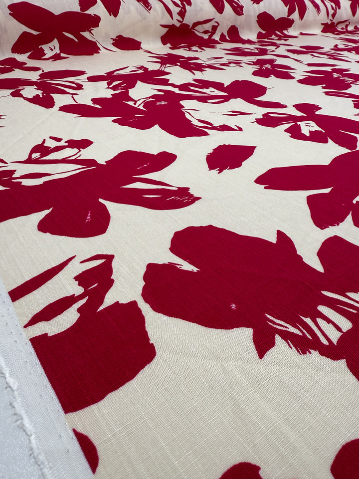 A close-up of Super Cheap Fabrics’ Bamboo Rayon - Crimson Bloom (150cm), displaying bold red abstract florals on cream. Lightweight, beginner-friendly, and partially unrolled for easy sewing.