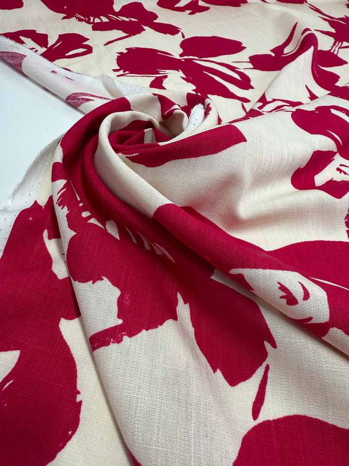 A close-up of Super Cheap Fabrics' Bamboo Rayon - Crimson Bloom (150cm), a lightweight, cream-colored fabric with large bold red floral prints, gently gathered into soft folds on a flat surface.