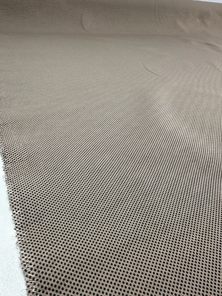 Close-up of Super Cheap Fabrics' Printed Bengaline - Pin Dot Sand, 150cm. It features light brown, medium-weight stretch fabric with small black dots. The smooth texture laid flat reveals depth and a slight curve, emphasizing its structured yet comfortable feel.
