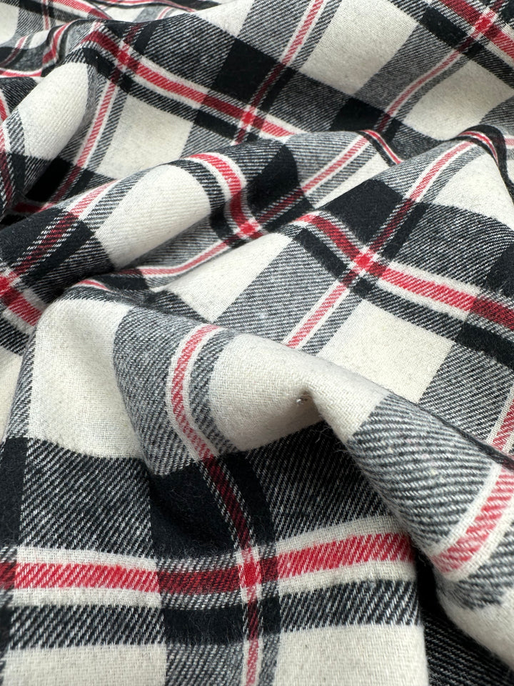 A close-up of Super Cheap Fabrics' Suiting - Black Watch Plaid (147cm) shows its soft cotton polyester twill in black, white, red, and gray with crisp folds and detailed texture.