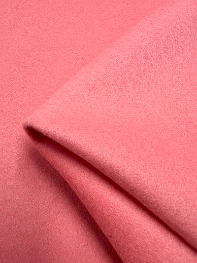 Close-up image of a folded piece of soft, pink Wool Cashmere - Shell Pink. The material appears smooth and has a slight sheen in the light, perfect for creating luxurious outer coats. This premium fabric is brought to you by Super Cheap Fabrics and measures 150cm in width.