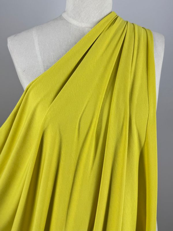 Close-up of a green, one-shoulder dress on a mannequin. Made from Super Cheap Fabrics' Cotton Lycra - Green Sheen - 170cm, it drapes gently with soft, flowing material and subtle sheen for an elegant look.