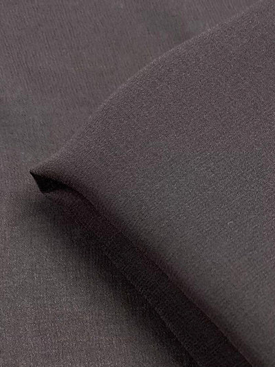 A close-up image of the Silk Georgette - Pewter - 135cm from Super Cheap Fabrics reveals the smooth texture of its dark gray fabric. Folded edges of this lightweight material create subtle shadows, showcasing its soft and uniform weave.