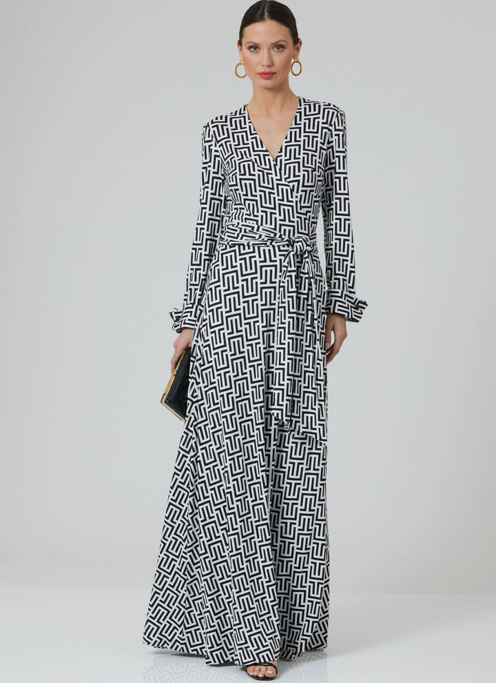 A woman poses against a plain background wearing the Pattern - Vogue - V2000 - Misses’ DVF Wrap Dress by Diane von Furstenberg from Super Cheap Fabrics, featuring long sleeves and a black and white geometric design, paired with hoop earrings and a clutch.
